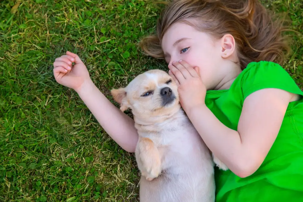A little girl laying on the grass with her dog.