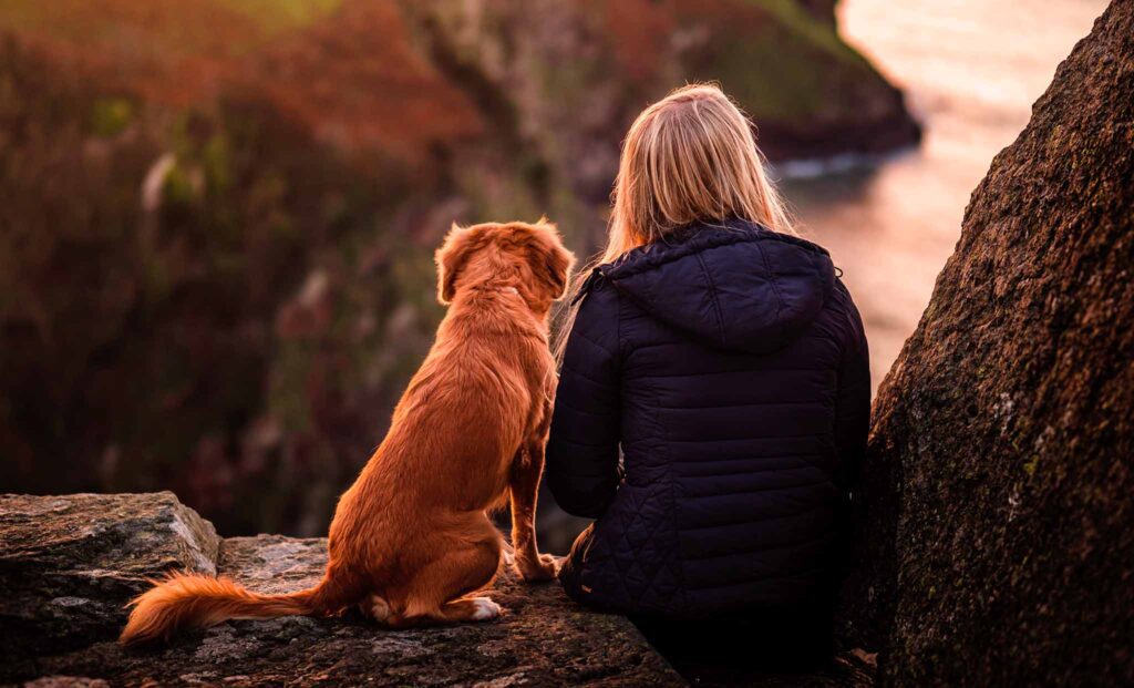 A woman sitting on the side of a cliff with her dog.