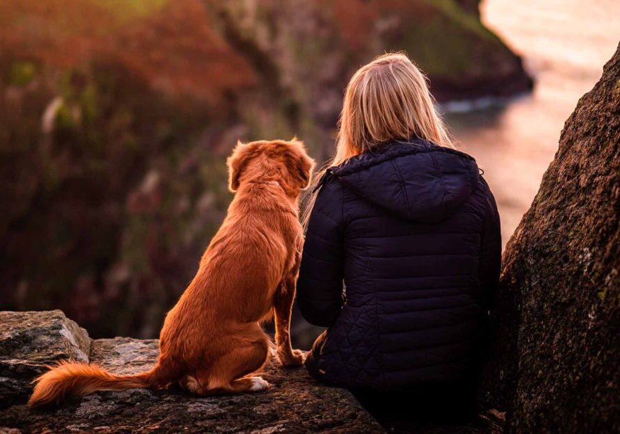 A woman sitting on the side of a cliff with her dog.